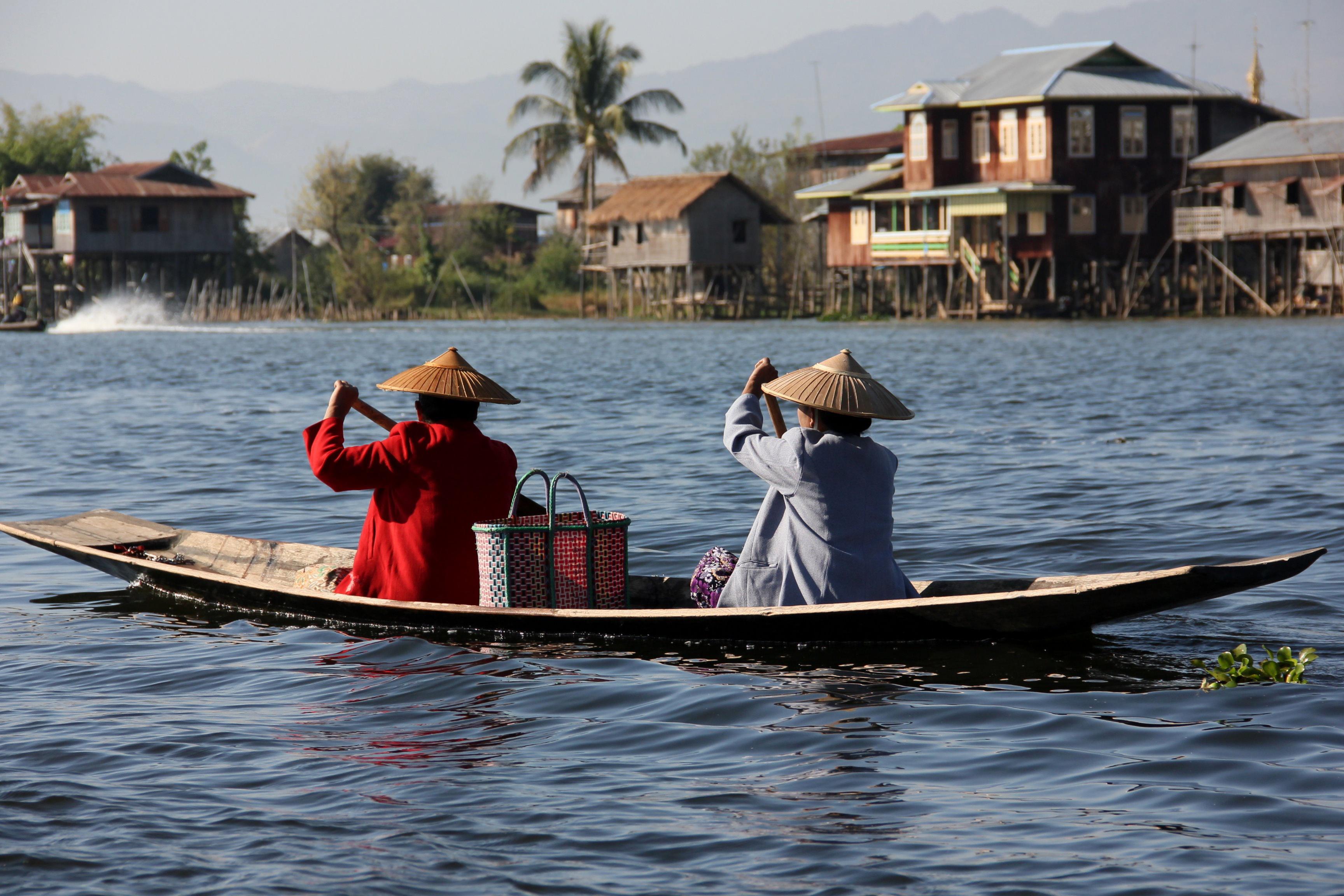 A traditional Inle Lake fisherman using the unique leg-rowing technique on a wooden boat at dawn.